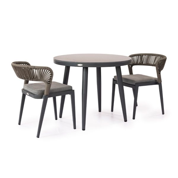 Conjunto de mesa de comedor minimalista con cubierta redonda y patas metálicas negras, acompañado de dos sillas tejidas en tono gris con cojines.